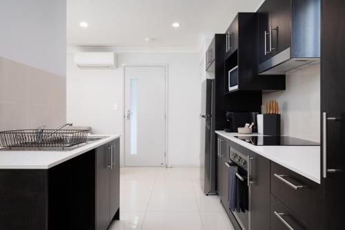 a kitchen with black cabinets and a white floor at Neatly Presented,Air Con and Modern! in Brisbane