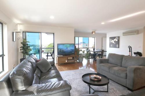 a living room with a leather couch and a television at Beech Break - 3 bedroom pet friendly apartment in Merimbula