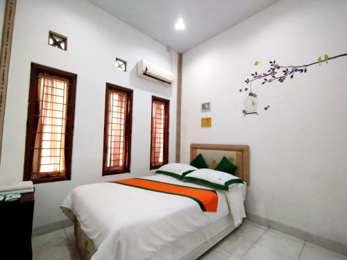 a white bedroom with a bed and windows at Homestay Jogja Dekat Taman Pelangi by Simply Homy in Yogyakarta