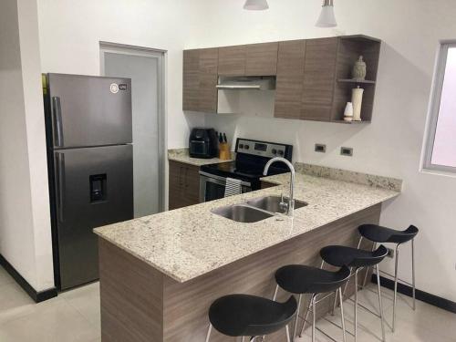 eine Küche mit einer Theke mit Hockern und einem Kühlschrank in der Unterkunft Hermoso Apartamento en Alajuela in Alajuela