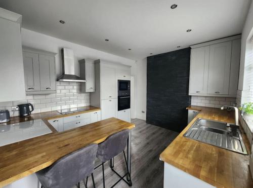 a kitchen with white cabinets and a wooden counter top at Cosy Worsley Home with a Garden Bar! in Manchester