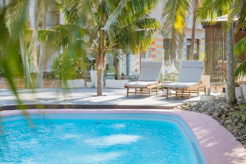 a swimming pool with two chairs and palm trees at The Med Crescent Head in Crescent Head