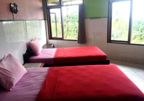 Habitación con 2 camas, sábanas rojas y ventanas. en Hotel Agung Putra, en Banyumas