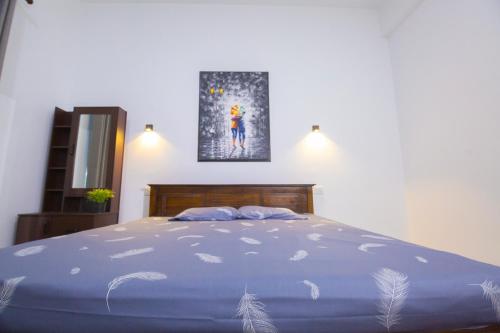ein Schlafzimmer mit einem blauen Bett und einem Gemälde an der Wand in der Unterkunft Artic Holiday Homes-Apartments in Weliweriya