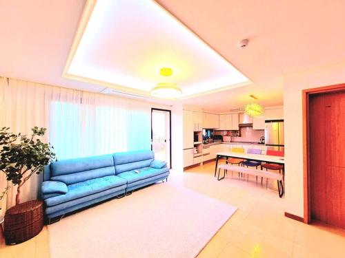 Una sala de estar con un sofá azul y una cocina. en Siyoung's House, en Jeju