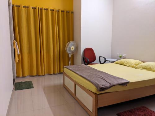 a bedroom with a bed with yellow curtains and a fan at Athreyas@60/A in Mysore
