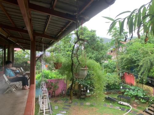 a man sitting in a chair on a porch looking at a garden at Homestay Bản Búa in Mộc Châu