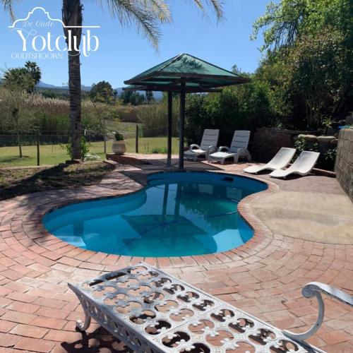 a small pool with chairs and an umbrella at De Oude Yotclub in Oudtshoorn