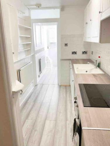 a kitchen with white cabinets and a wooden floor at Lovely Two Bedroom Apartment, with private garden! in Torquay