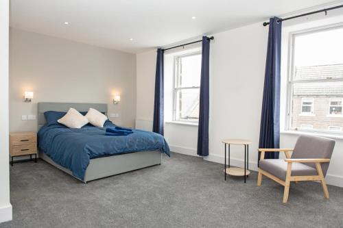 a bedroom with a bed and a chair and two windows at Cara Lodge, Comfortable Self Check-in En-suite Guest Rooms in Berwick-Upon-Tweed