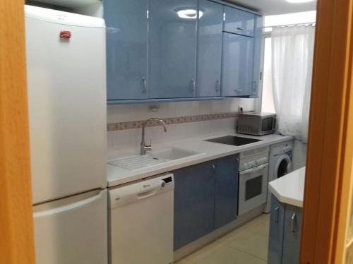 eine Küche mit blauen Schränken und einem weißen Kühlschrank in der Unterkunft Apartamento en playa de Valdelagrana in El Puerto de Santa María