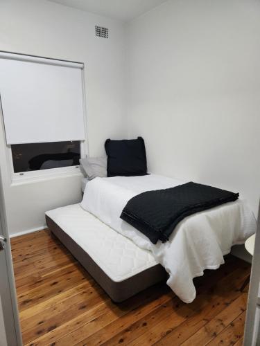 a white bedroom with a bed with a black blanket at Peaceful Getaway! in Sydney