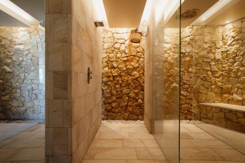 a bathroom with a walk in shower next to a stone wall at Poiano Garda Resort Appartamenti in Garda