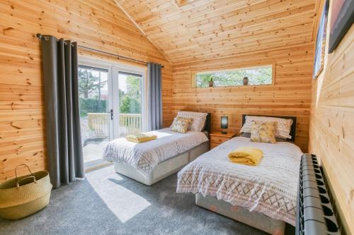 two beds in a log cabin bedroom with a window at Bwthyn Gwyn in Benllech