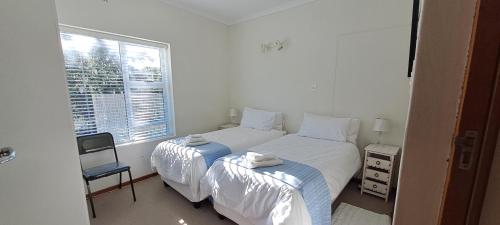 a white bedroom with two beds and a window at Rus en Vrede in De Kelders
