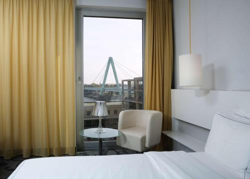 ケルンにあるart'otel cologne, Powered by Radisson Hotelsのベッド1台、椅子、窓が備わる客室です。