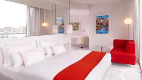 a bedroom with a large bed and a red chair at art'otel cologne, Powered by Radisson Hotels in Cologne