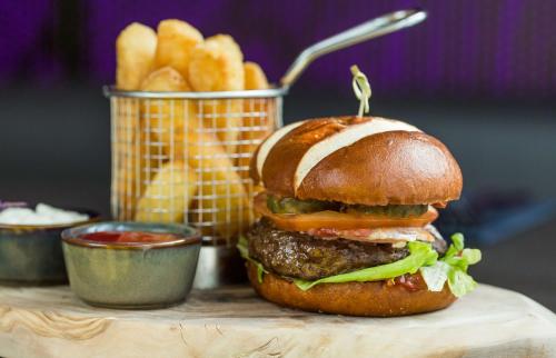 a hamburger on a table with fries and a basket of ketchup at Park Plaza London, Park Royal in London