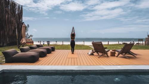 a woman standing in a yoga pose on a deck near the beach at LalaGalu - Beachfront EcoCabins in Diani Beach