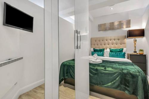 um quarto com uma cama com lençóis verdes e uma televisão em Modern One Bed Serviced Apartment in Chelsea em Londres