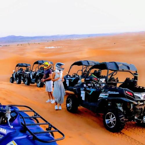 a group of people standing in the desert with four atvs at Riad Berber Merzouga in Merzouga