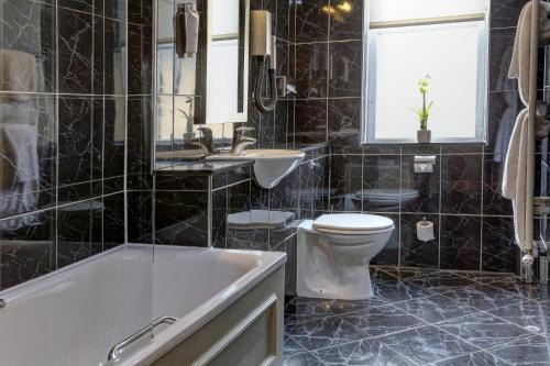 a black tiled bathroom with a tub and a toilet at The Midland Hotel in Bradford