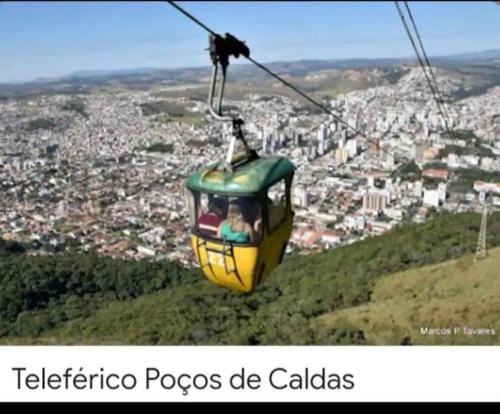 a yellow and green cable car flying over a city at Apartamento ao lado Praça Central in Poços de Caldas