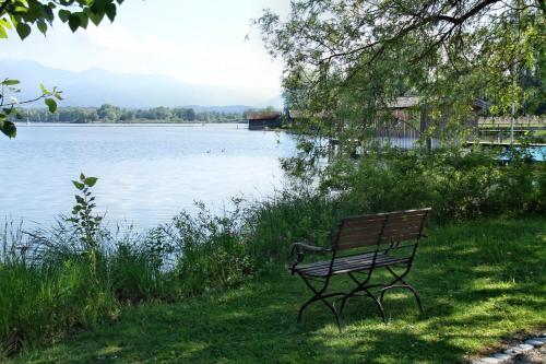 Hotel Aiterbach am Chiemsee في ريمستينغ: مقعد حديقة يجلس على العشب بالقرب من بحيرة