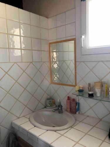 a white tiled bathroom with a sink and a mirror at Agréable T2 avec toit terrasse face à la plage in Sausset-les-Pins