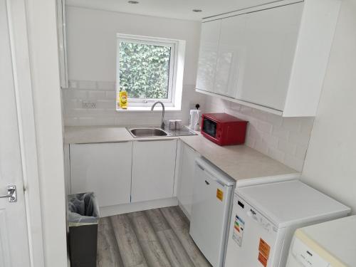 a white kitchen with a sink and a red microwave at Holiday Out House in London