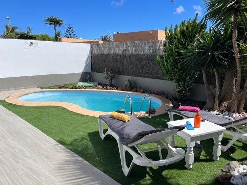 einen Hinterhof mit einem Pool mit Stühlen und einem Tisch in der Unterkunft Villa Papi in La Oliva