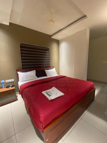 a bedroom with a red bed with a book on it at Redbell Suites Kizhisseri in Kondotti