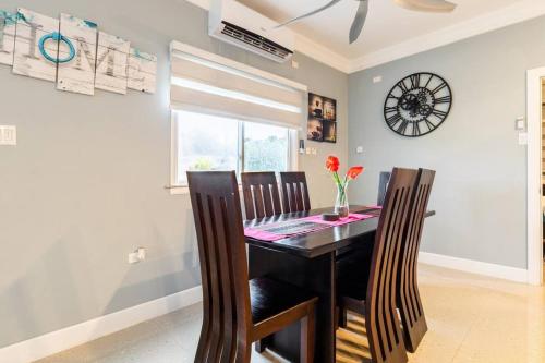 a dining room table with chairs and a clock on the wall at serendipity on the beach Ocho Rios in Saint Annʼs Bay