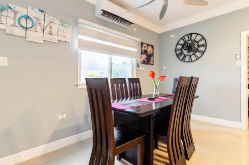 a dining room table with chairs and a clock on the wall at serendipity on the beach Ocho Rios in Saint Annʼs Bay