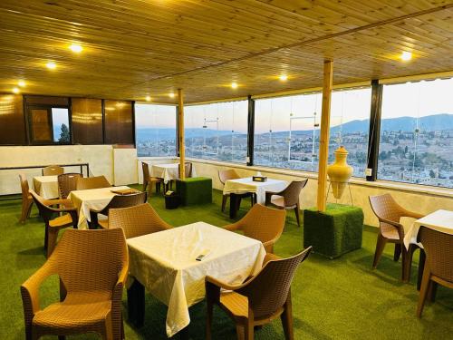 un restaurante con mesas, sillas y ventanas grandes en Dream house hotel jerash, en Jerash