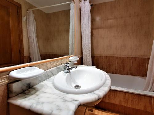 a bathroom with a white sink and a bath tub at Apartamentos SOL Y PLAYA Foz in Foz
