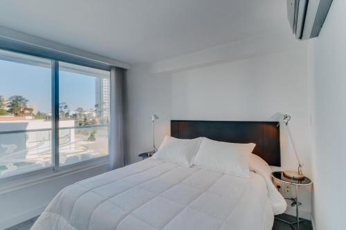 um quarto com uma cama branca e uma grande janela em Oceana Suites en Yoo, con piscina interior climatizada em Punta del Este