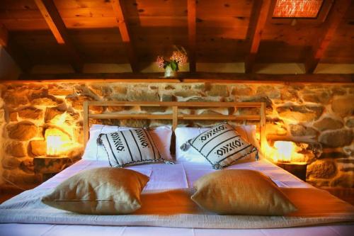 - un lit avec des oreillers dans une chambre dotée d'un mur en pierre dans l'établissement Dríade, à Villar de las Traviesas