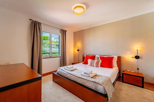 a bedroom with a bed with red pillows and a window at Garajau Ocean Garden View in Caniço