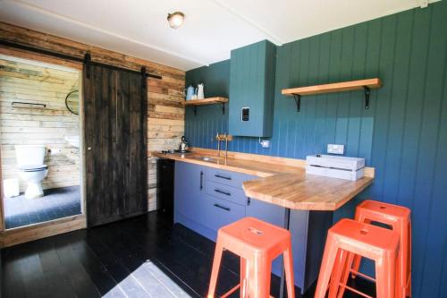 a kitchen with a wooden counter and two orange stools at The Hambleton Hut in Upper Hambleton