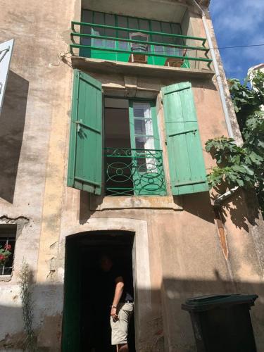 a man standing in a doorway of a building with a green window at Byhus - det genuina Frankrike in Laurens