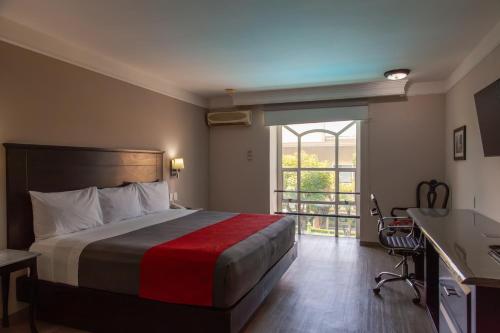 a hotel room with a bed and a desk and a window at Plaza Camelinas Hotel in Querétaro