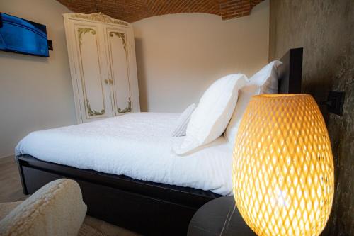 a bedroom with a bed with white sheets and a lamp at Le camere del Cappello Verde in Ivrea