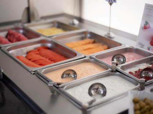 a kitchen counter with trays of different types of food at Ramada Encore by Wyndham Queretaro in Querétaro