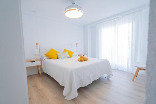 ein weißes Schlafzimmer mit einem weißen Bett und gelben Kissen in der Unterkunft Apartamento en Gran Playa in Santa Pola