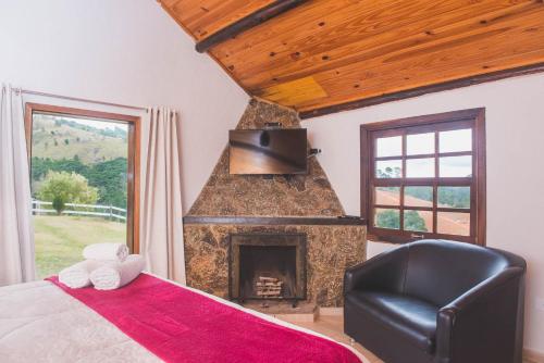 a bedroom with a fireplace and a bed with a chair at Chales Boa Vista in Monte Verde