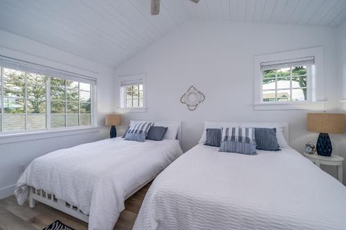 two beds in a bedroom with white walls and windows at Hydrangea House in Seaside