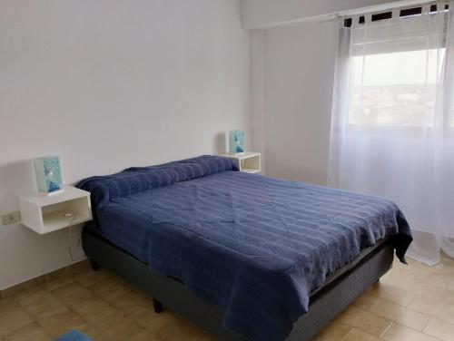 a bedroom with a bed with a blue comforter and a window at Bravard suites in Bahía Blanca