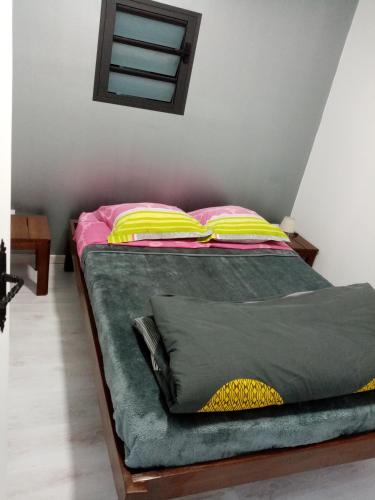 a bed with pink and yellow pillows in a room at studio meublé près de la mare à joncs in Cilaos