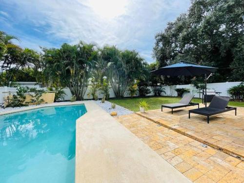 una piscina con 2 sillas y una sombrilla en Tropical Oasis House Private Pool Family Yard en Fort Lauderdale